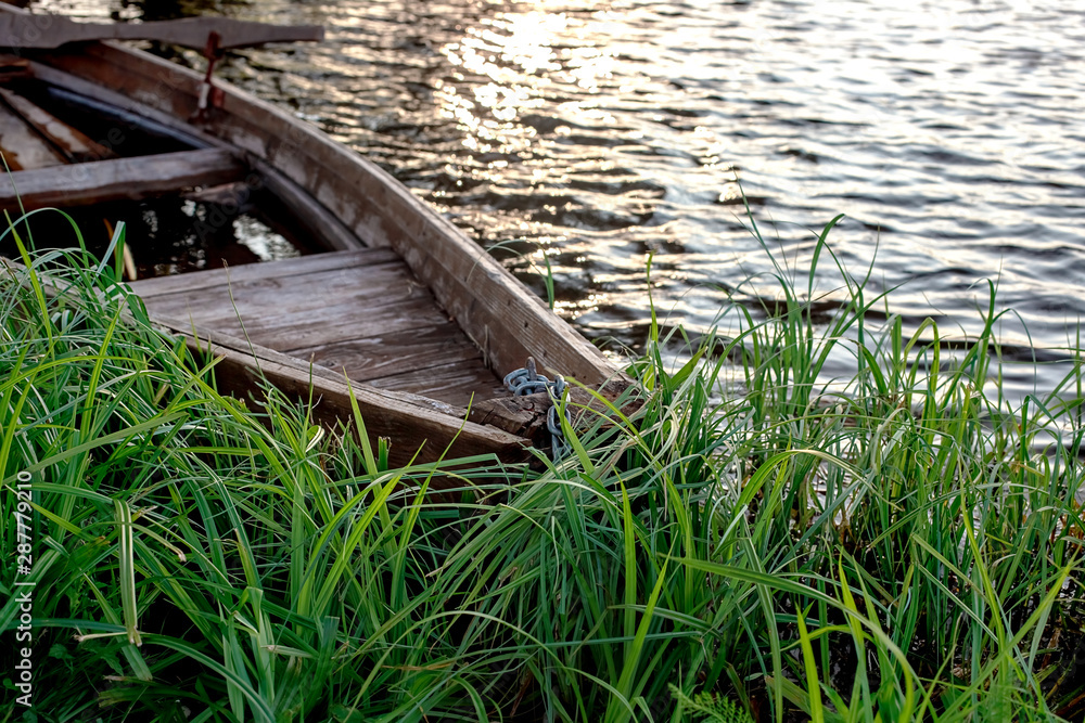 A small wooden rowing boat with a broken bottom on a calm lake near the shore. A small wooden rowing boat with a broken bottom on a calm lake near the shore.