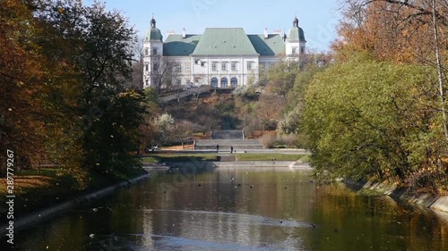 City park Royal Lazienki with pond or lake and  Ujazdowski Castle on background with blue sky, trees and fallen leaves at autumn. Warsaw, Poland, Europe. Camera move from bottom to top photo