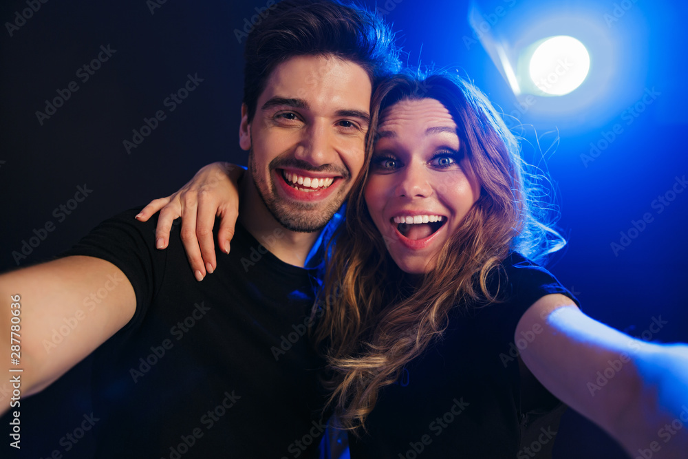 Foto Stock Pleased young loving couple having fun resting in a night disco  club on concert take selfie by camera. | Adobe Stock