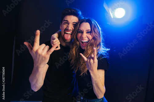 Loving couple having fun resting in a night disco club on concert showing rock gesture.