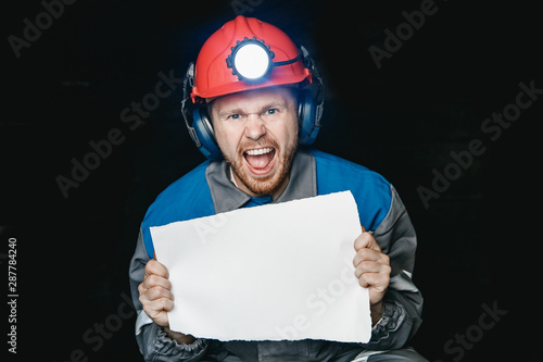 Miner angry man screams and frowns, holds sheet of paper for text. Concept mining strike uprising © Parilov