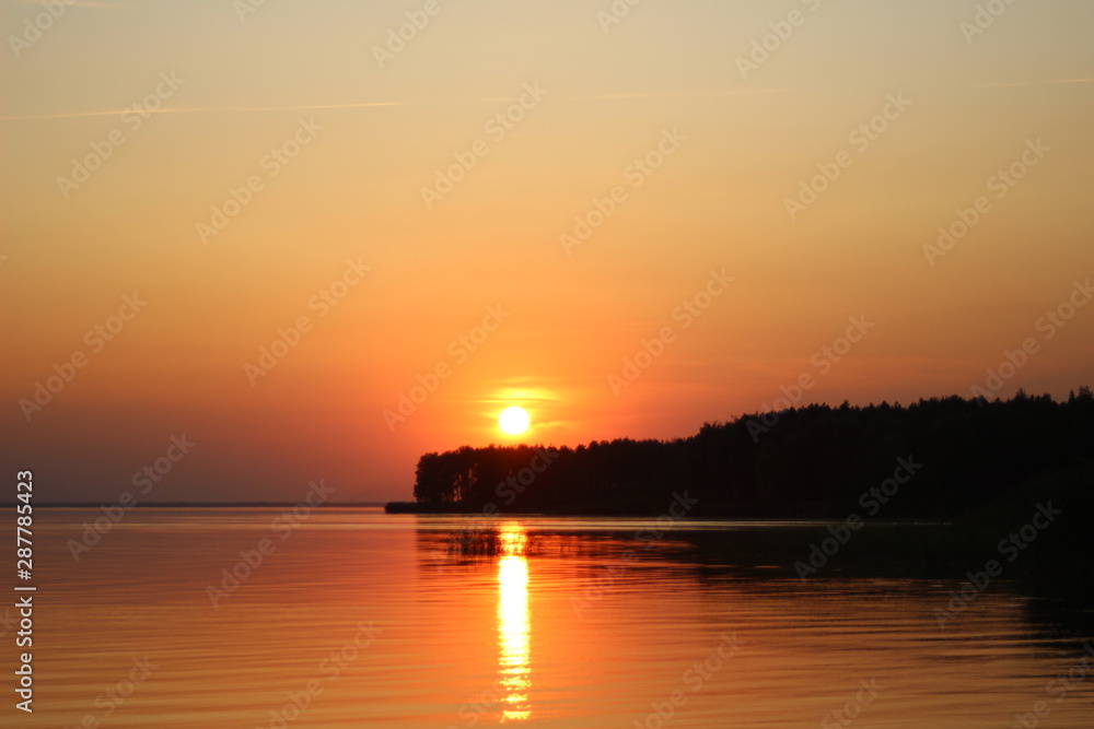 The  horizontal photo of golden sunset above the river or sea. Reflection in the water like fire. Seacoast.
