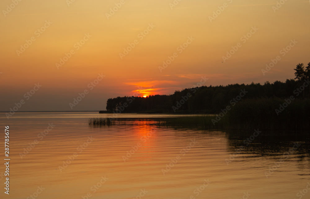 The  horizontal photo of golden sunset above the river or sea. Reflection in the water like fire. Seacoast.