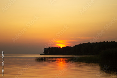 The horizontal photo of golden sunset above the river or sea. Reflection in the water like fire. Seacoast.