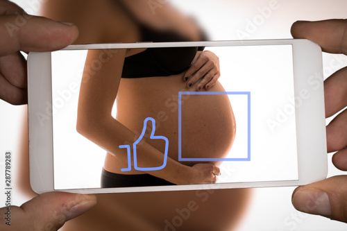 Sharenting or overuse of social media by parents to share content about their children concept: taking a photo of a woman's pregnant belly