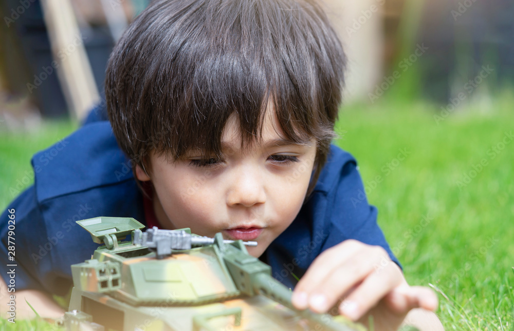 Active boy laying down on the grass playing with soldiers and tank toys in the garden,Kid playing wars and peace on his own in hot sunny day,Children imagination and development Active boy laying down on the grass playing with soldiers and tank toys in the garden,Kid playing wars and peace on his own in hot sunny day,Children imagination and development