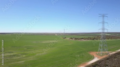 Aerial panoramic view of flight along high voltage power line in rural countryside of Western Australia, with blue sky and horizon as background.