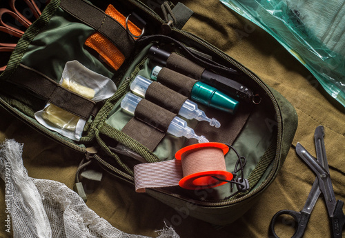 Open first aid kit with drugs and medical instruments on olive textile background. First aid in an emergency