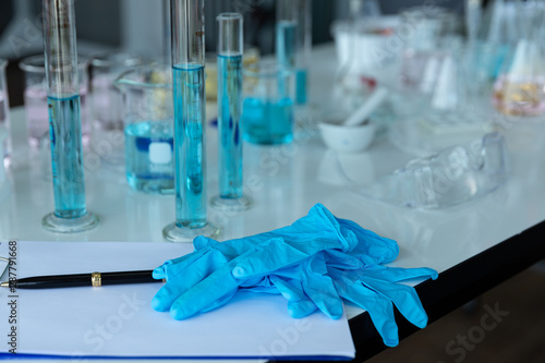 In lap at university science chemistry concept. Laboratory test tubes and flasks with color liquid put on white table for work check and test chemistry.blue glove take off on table in relax time.