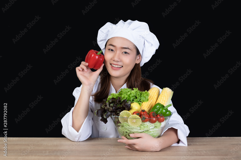 Portrait of a young beautiful Asian woman chef smiling and preparing ingredients for meal or salad. She was happy and confident .Half figured, Isolated and studio lighting on black background. Portrait of a young beautiful Asian woman chef smiling and preparing ingredients for meal or salad. She was happy and confident .Half figured, Isolated and studio lighting on black background.