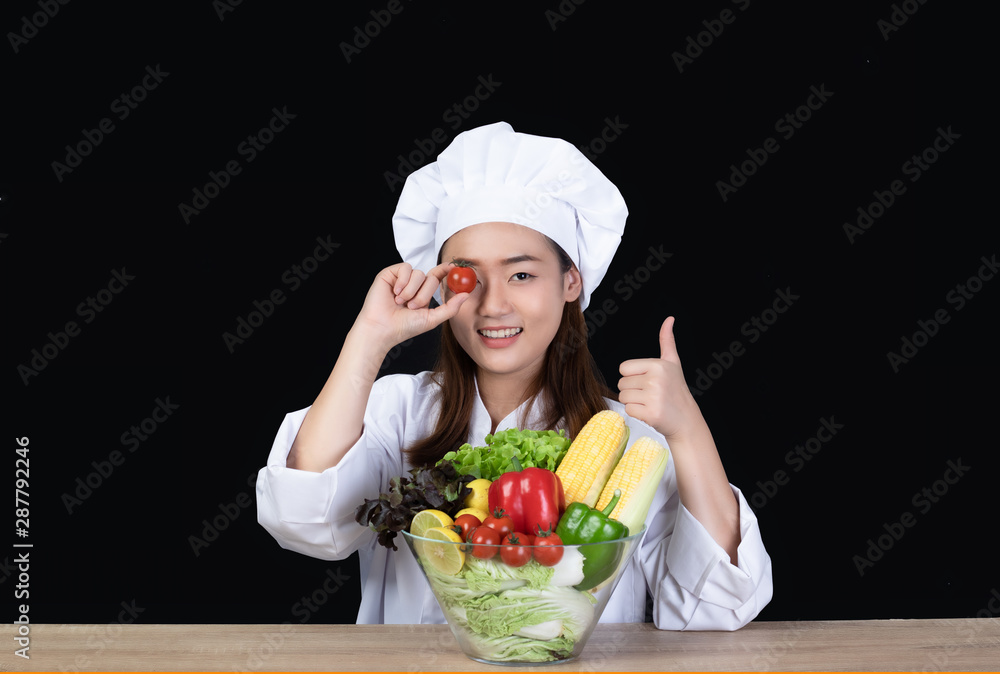Portrait of a young beautiful Asian woman chef smiling and preparing ingredients for meal or salad. She was happy and confident .Half figured, Isolated and studio lighting on black background. Portrait of a young beautiful Asian woman chef smiling and preparing ingredients for meal or salad. She was happy and confident .Half figured, Isolated and studio lighting on black background.