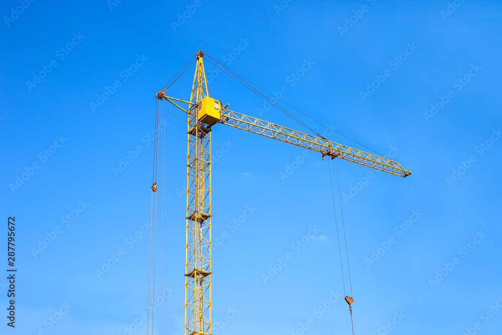 Construction crane tower on blue sky background. Crane and building working progress. Yellow lifting faucet. Empty Space for text. Construction concept. Site. New buildings with a crane. Tower crane Construction crane tower on blue sky background. Crane and building working progress. Yellow lifting faucet. Empty Space for text. Construction concept. Site. New buildings with a crane. Tower crane