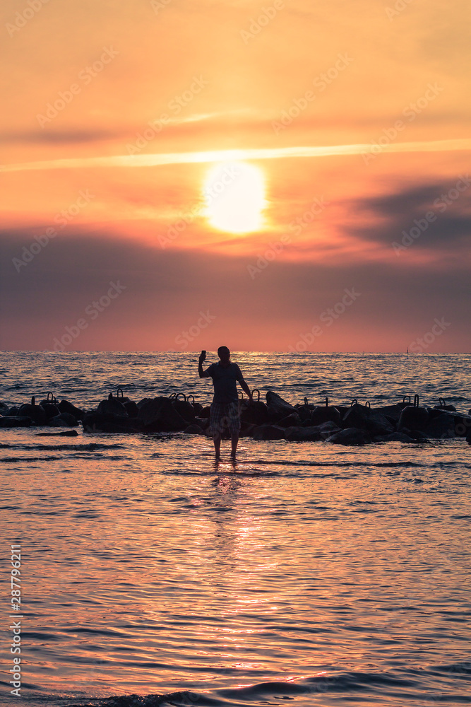 One man making  a sselfie in the sea during sunset