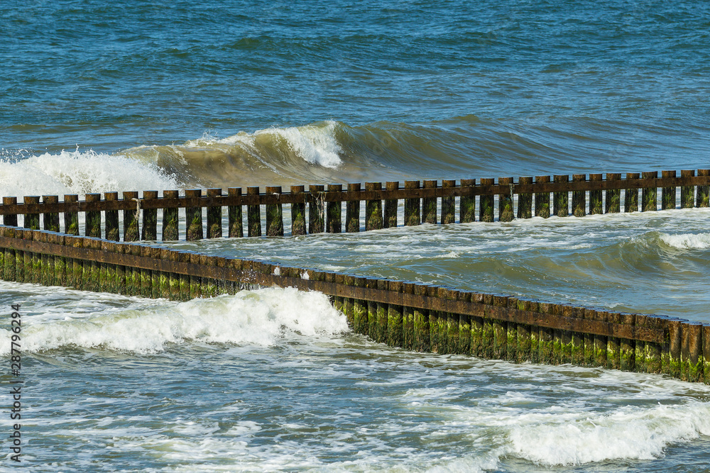Seascape with waves crashing the wooden poles breakwater on a sunny day.