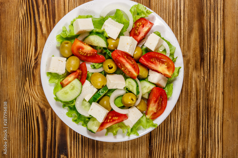 Greek salad with fresh vegetables, feta cheese and green olives on wooden table. Top view Greek salad with fresh vegetables, feta cheese and green olives on wooden table. Top view