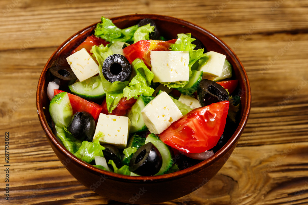 Greek salad with fresh vegetables, feta cheese and black olives on wooden table