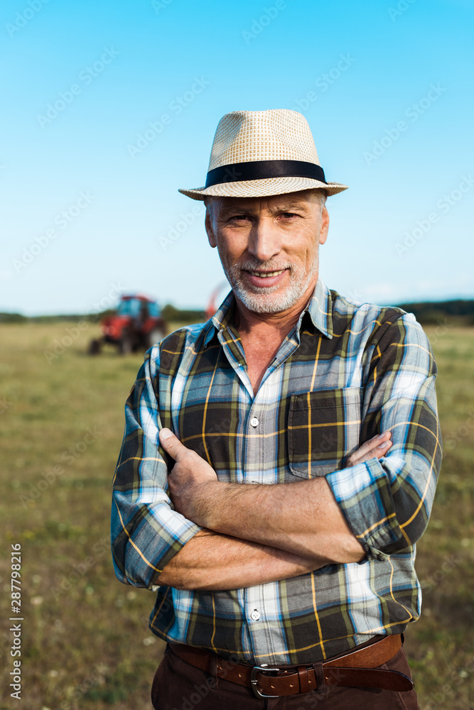 cheerful senior farmer standing with crossed arms in field