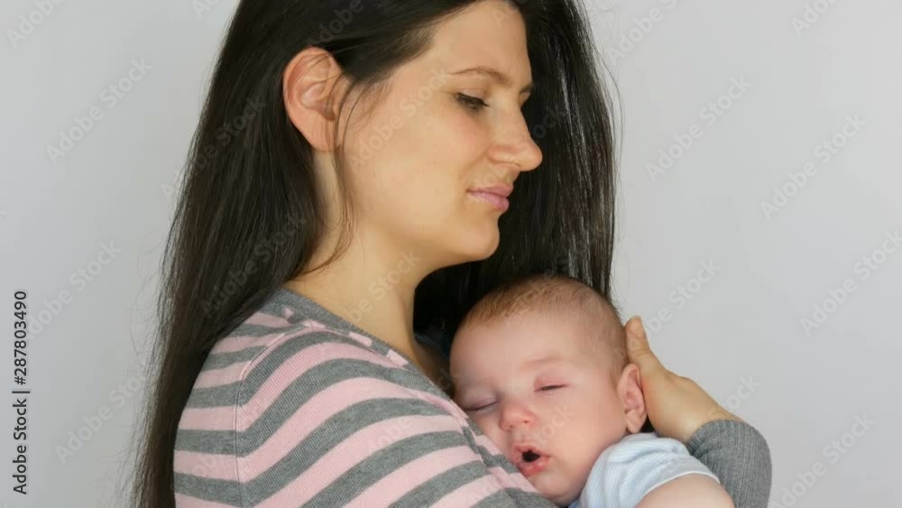 Young beautiful mother with long dark hair is holding a newborn infant baby of two months on a white background in studio Young beautiful mother with long dark hair is holding a newborn infant baby of two months on a white background in studio