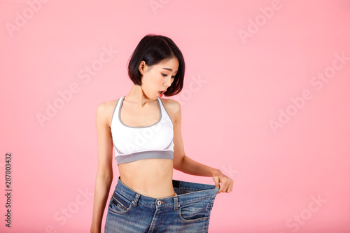Fit woman in oversize blue jeans on pastel pink background. Diet and weight loss concept.