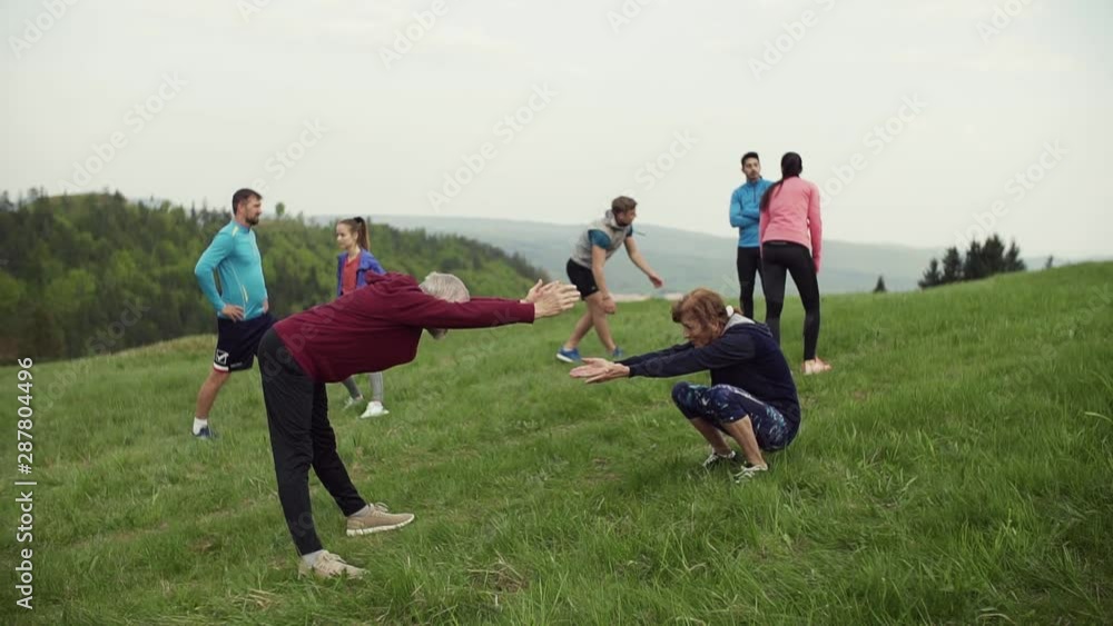 Large group of fit and active people doing exercise in nature, stretching.