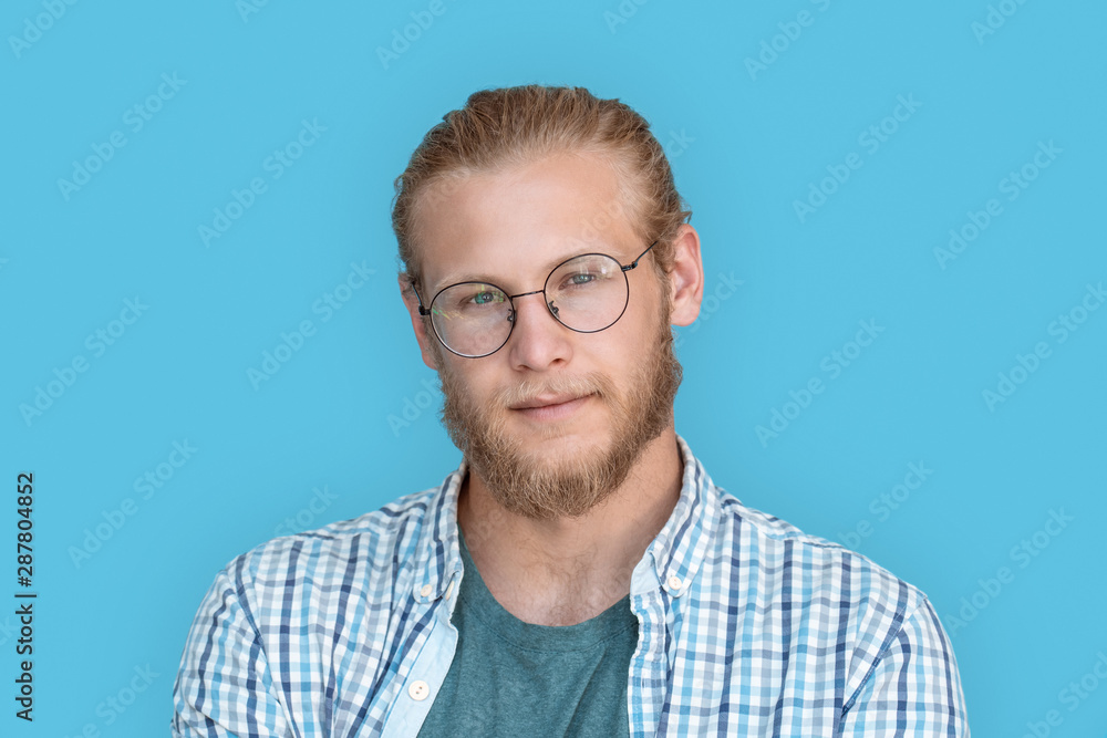 Young bearded handsome man blond hair hipster face wearing optical glasses looking at camera, millennial handsome casual guy isolated on blue studio blank background, close up view headshot portrait Young bearded handsome man blond hair hipster face wearing optical glasses looking at camera, millennial handsome casual guy isolated on blue studio blank background, close up view headshot portrait