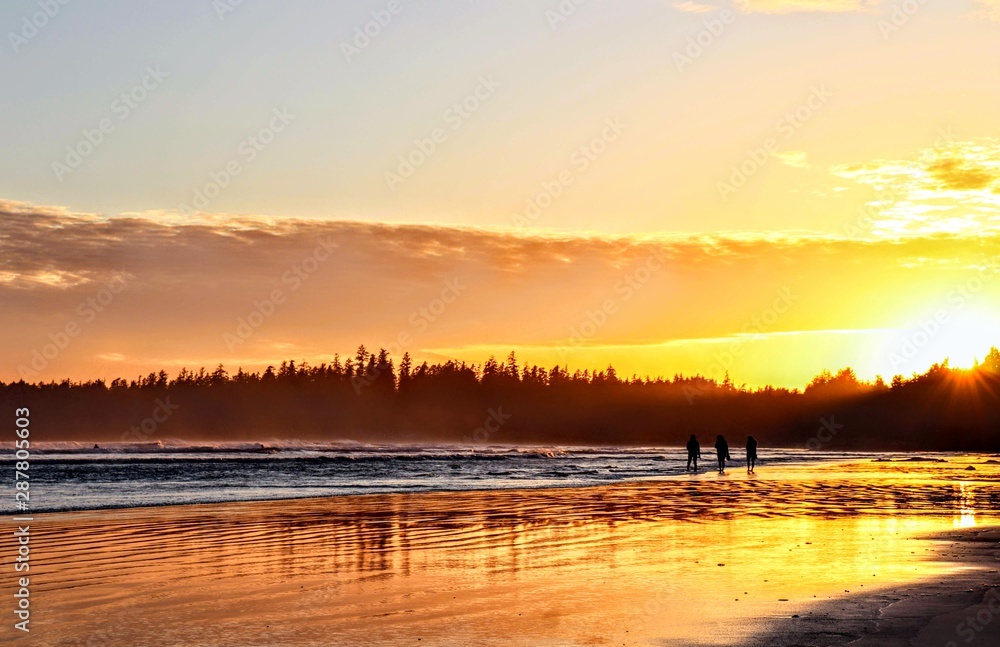 Obraz premium Silhouette people walking on the beach during the sunset at the edge of the ocean, surrounded by mountains