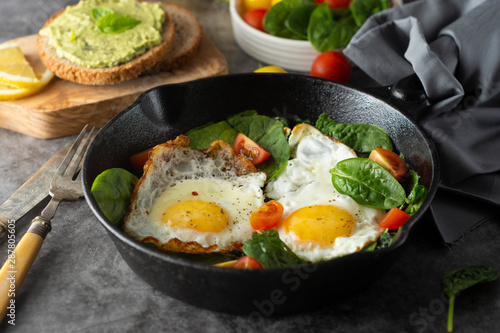 Fried sunny eggs with spinach, avocado toast and fresh tomatoes. healthy breakfast food.