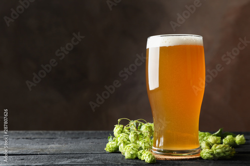 Glass of beer and hop cones on wooden table, copy space