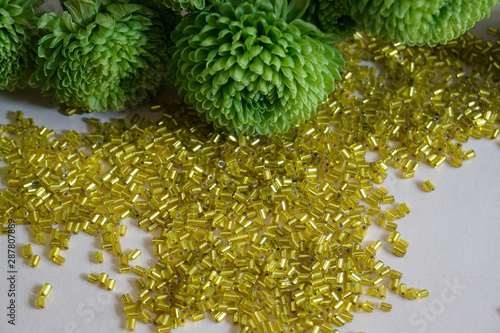Yellow tubular toho beads and green Chrysanthemum on light cream background. photo