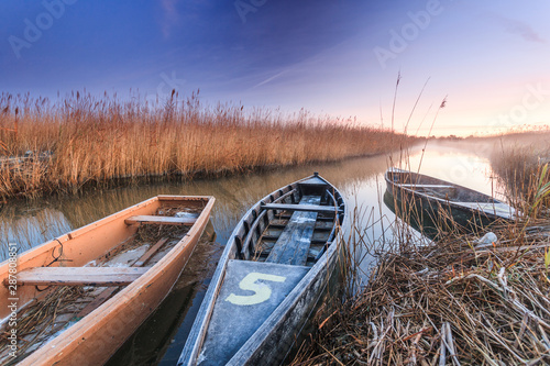 Holzboote an einem Fluss im Schilf im Ebro Delta nahe Barcelona in Spanien zu Sonnenaufgang