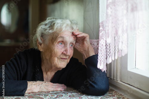 Elderly russian woman sits in a house near the window.