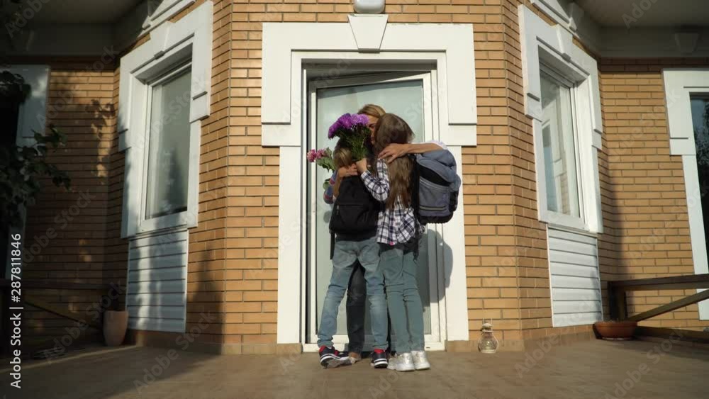Little cute boy and girl with backpacks coming home and bringing flowers for their mother. Happy loving family concept Little cute boy and girl with backpacks coming home and bringing flowers for their mother. Happy loving family concept
