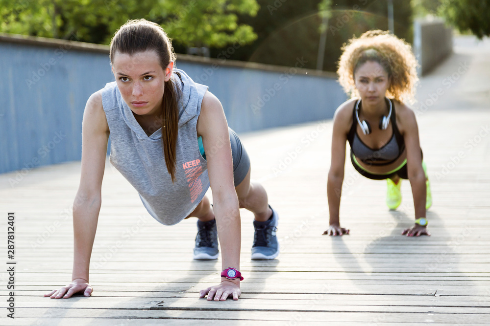 Two sporty young women doing push-ups on a bridge