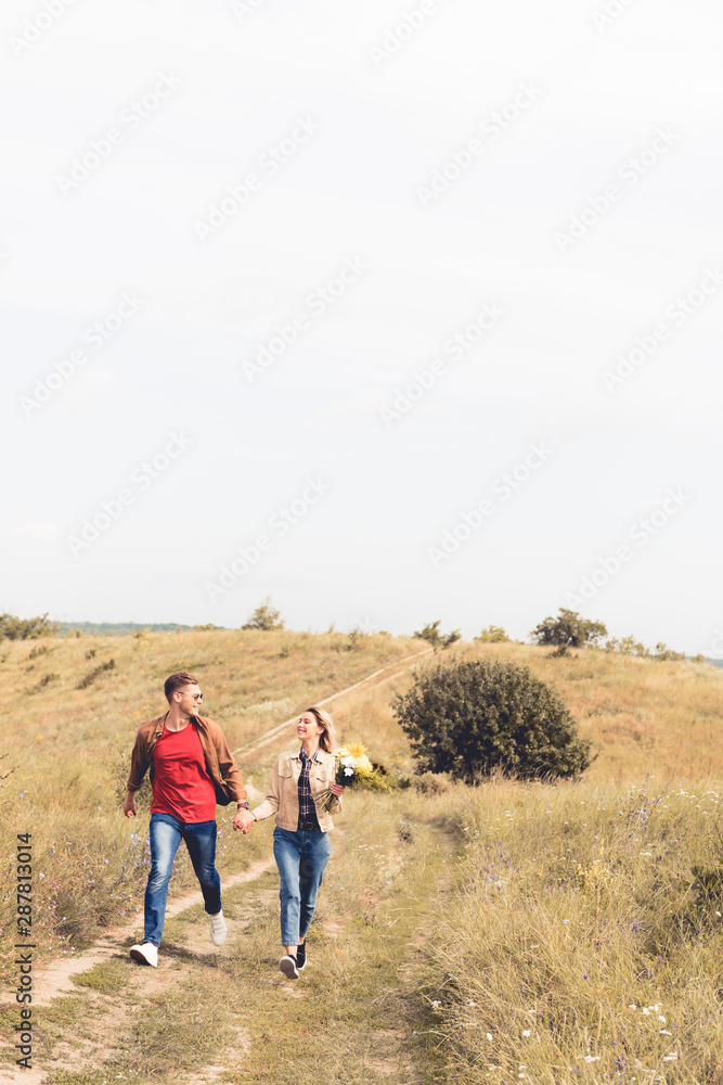 attractive woman with bouquet and handsome man smiling and holding hands