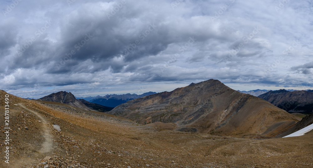Hiking trail through a panoramic Rocky Mountain landscape with a white clouds, mountains and hills.