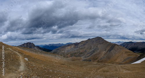 Hiking trail through a panoramic Rocky Mountain landscape with a white clouds, mountains and hills.