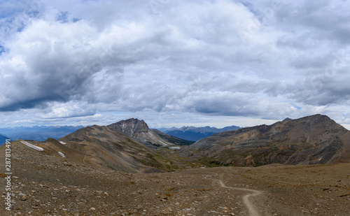 Quadro em tela Hiking trail through a panoramic Rocky Mountain landscape with a white clouds, mountains and hills