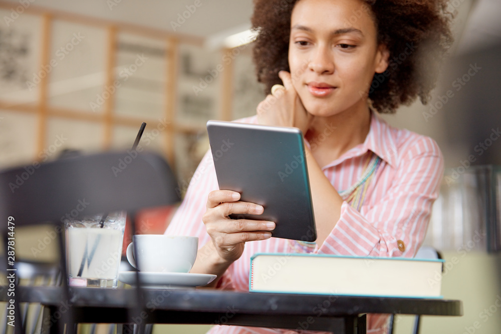 Attractive mixed race woman in striped pink dress sitting in cafe and using tablet. Attractive mixed race woman in striped pink dress sitting in cafe and using tablet.