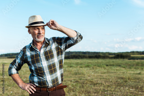 happy farmer standing with hand on hip while touching straw hat