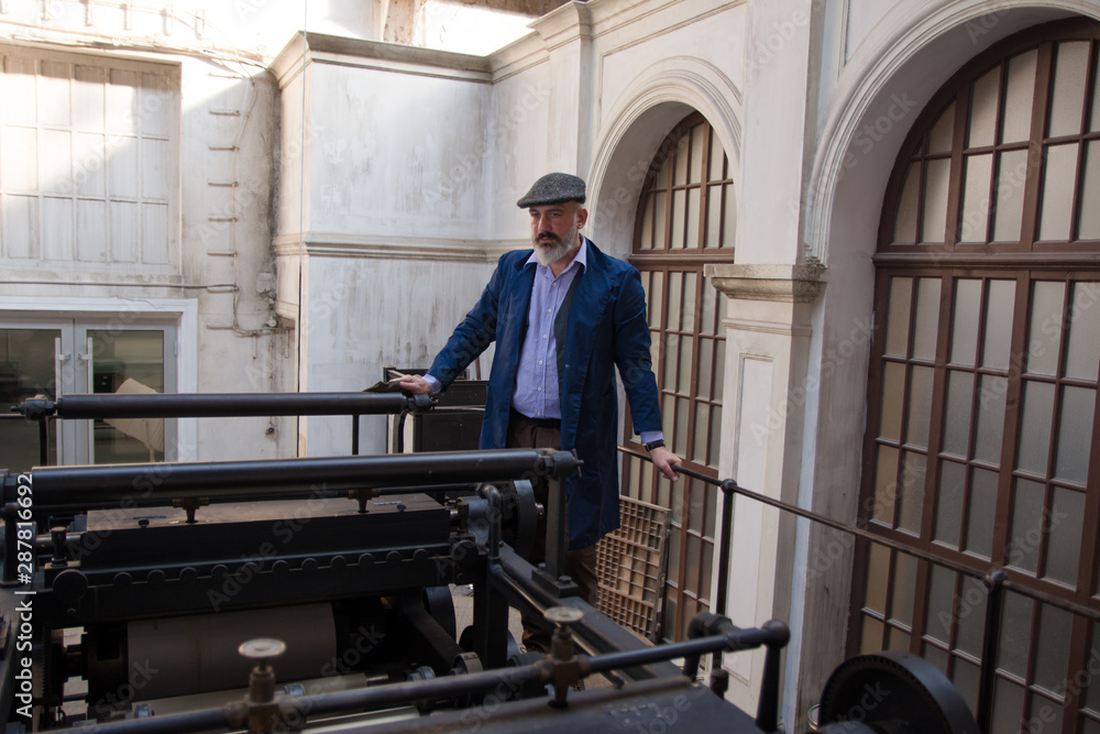 Fototapeta premium Worker standing on top platform of an old vintage press for newspaper printing