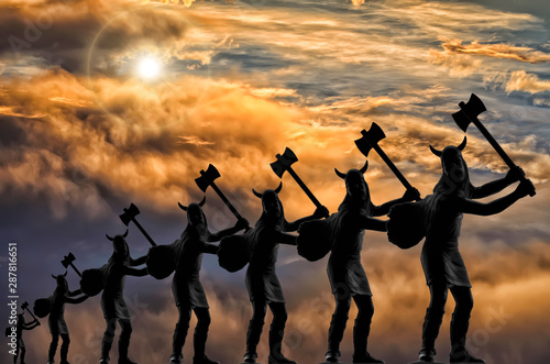 Seven silhouettes of attacking Vikings (plastic toy soldiers) with axes arrayed in a line, stormy sky with clouds, bright sun, vanishing point effect, Old Norse, Ragnarok, Valhalla and Odin themes