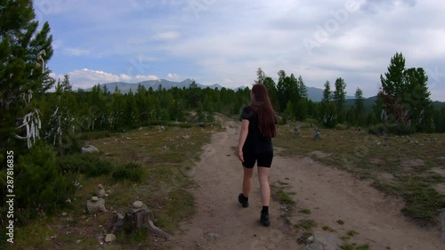 girl goes on a mystical abandoned path in the mountains. pyramids of stones, trees tied with ritual ribbons. slow motion video, rear view in motion