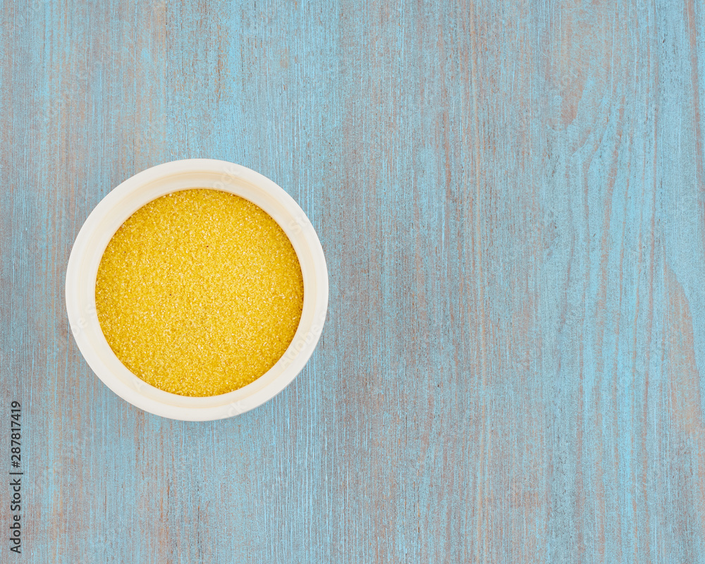 Yellow corn flour in white bowl on blue wooden table, ingredients for Polenta, gluten free, fodmap Yellow corn flour in white bowl on blue wooden table, ingredients for Polenta, gluten free, fodmap