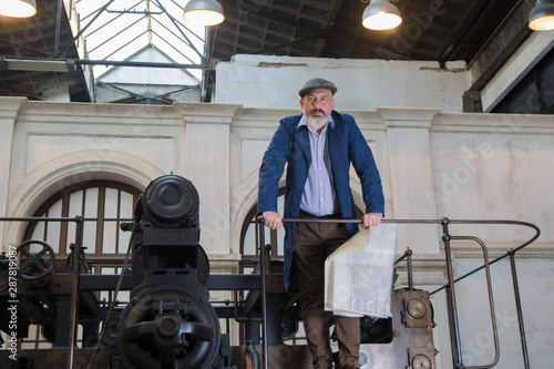 Worker standing on top platform of an old vintage press for newspaper printing