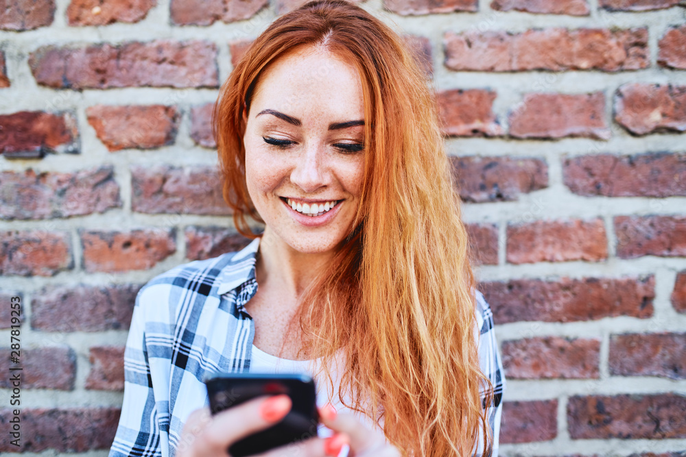 Young woman leaning against brick wall in the city while using smartphone Young woman leaning against brick wall in the city while using smartphone
