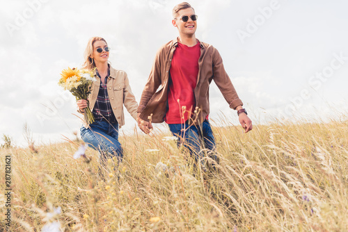 attractive woman and handsome man in sunglasses walking and holding hands