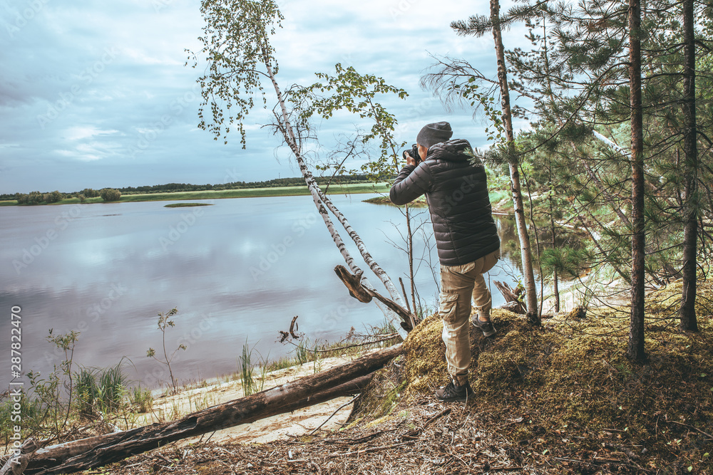 Naklejka premium A man in a gray jacket, take a photo of nature on the banks of the river, in the forest