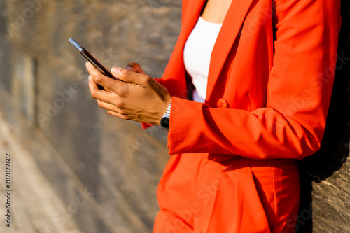 Woman wearing fashionable red pantsuit holding cell phone, partial view