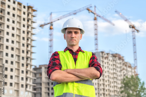 civil engineer in white helmets and a yellow vest on the background of the house under construction.