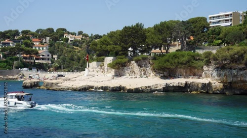 Rocky shore with unrecognizable people sunbathing on stony cliff. Irrecognizable yacht sailing in beautiful blue Mediterranean sea in Cassis, France photo